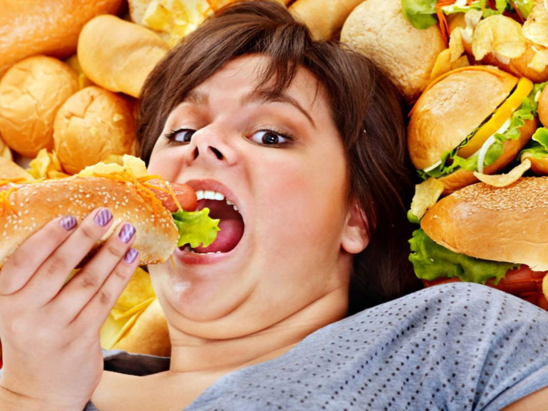 Полная женщина ест много фастфуда и переедает