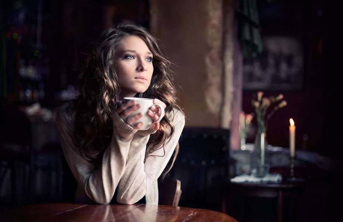 Девушка сидит в одиночестве и пьет чай или кофе