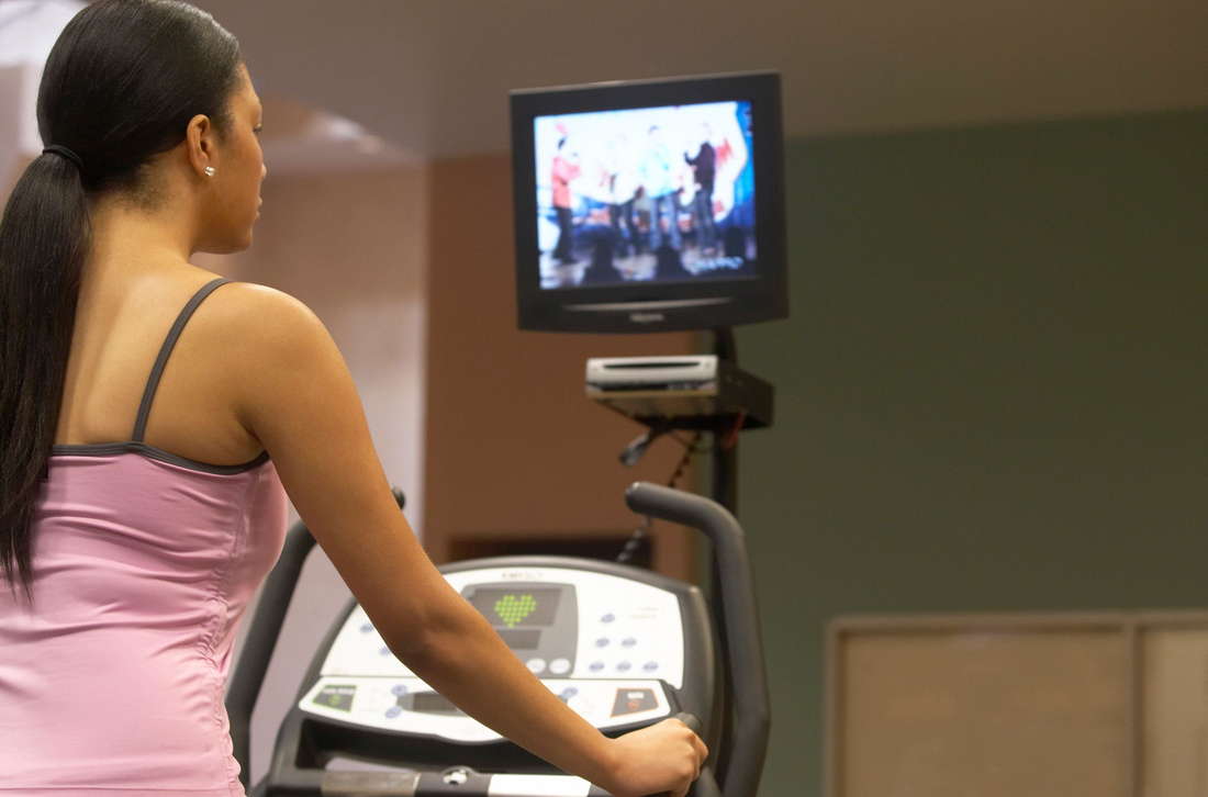 Девушка выполняет упражнения перед телевизором на беговой дорожке