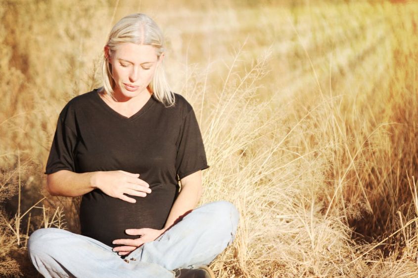 Беременная девушка сидит в поле