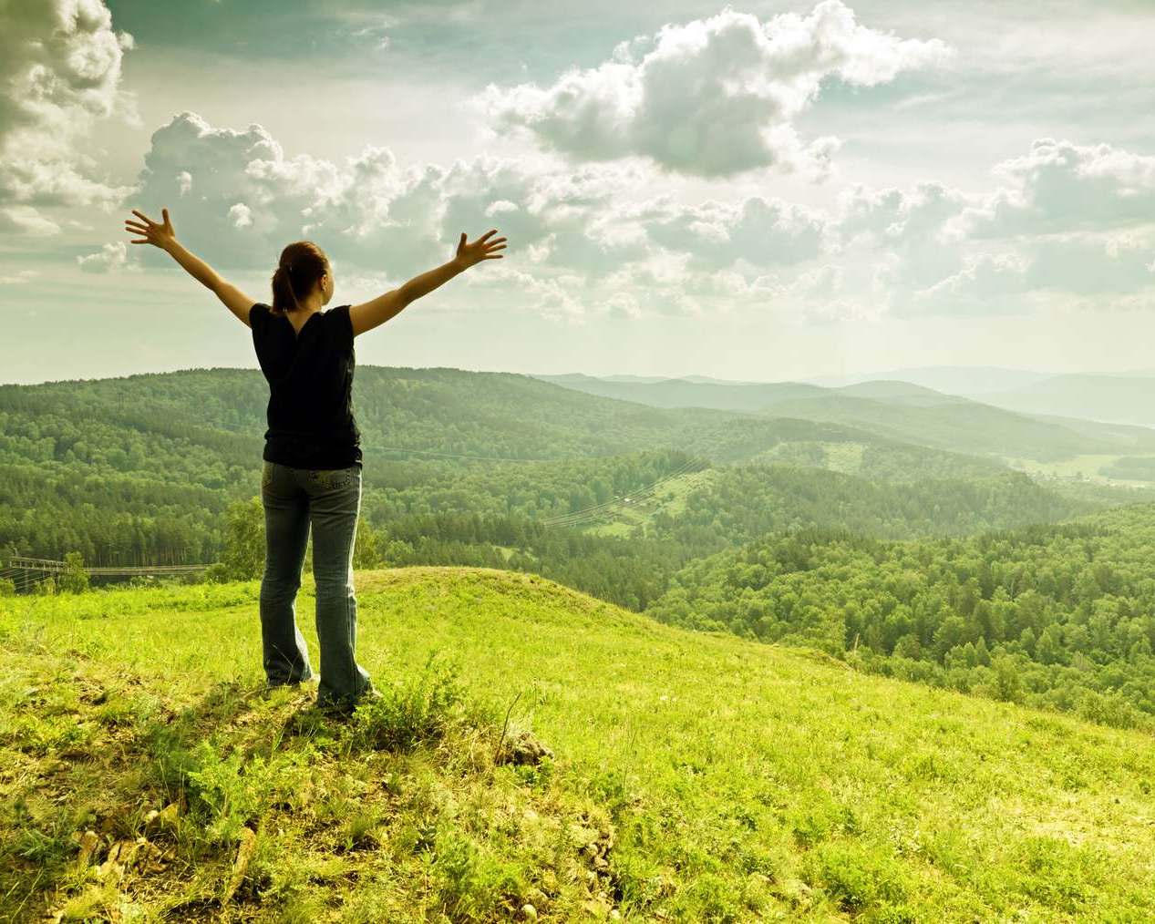 Девушка на зеленом холме наслаждается природой подняв руки