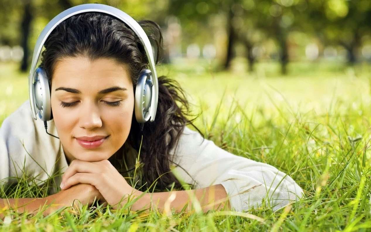 Девушка в наушниках слушает релаксирующую и успокаивающую музыку на траве
