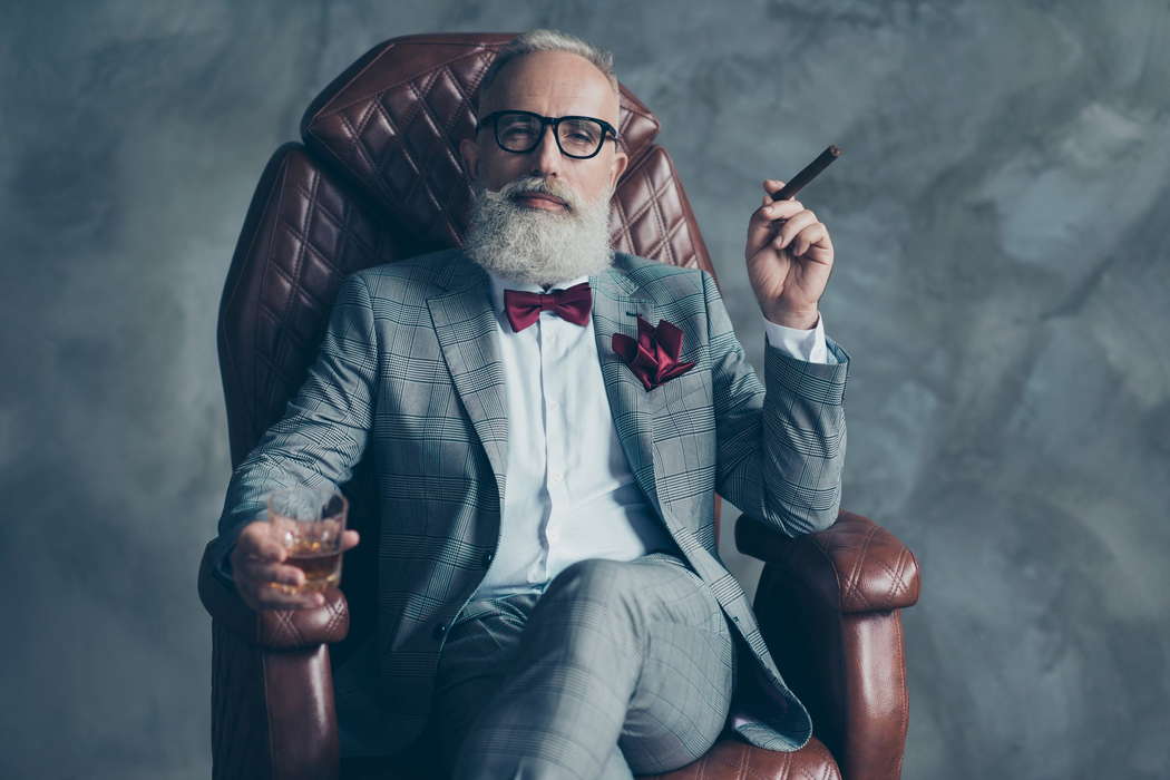 Богатый стильно одетый человек с сигарой и коньяком в кресле